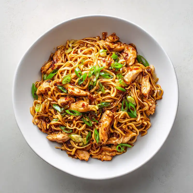 Sticky chili garlic chicken noodles with scallions in white plate