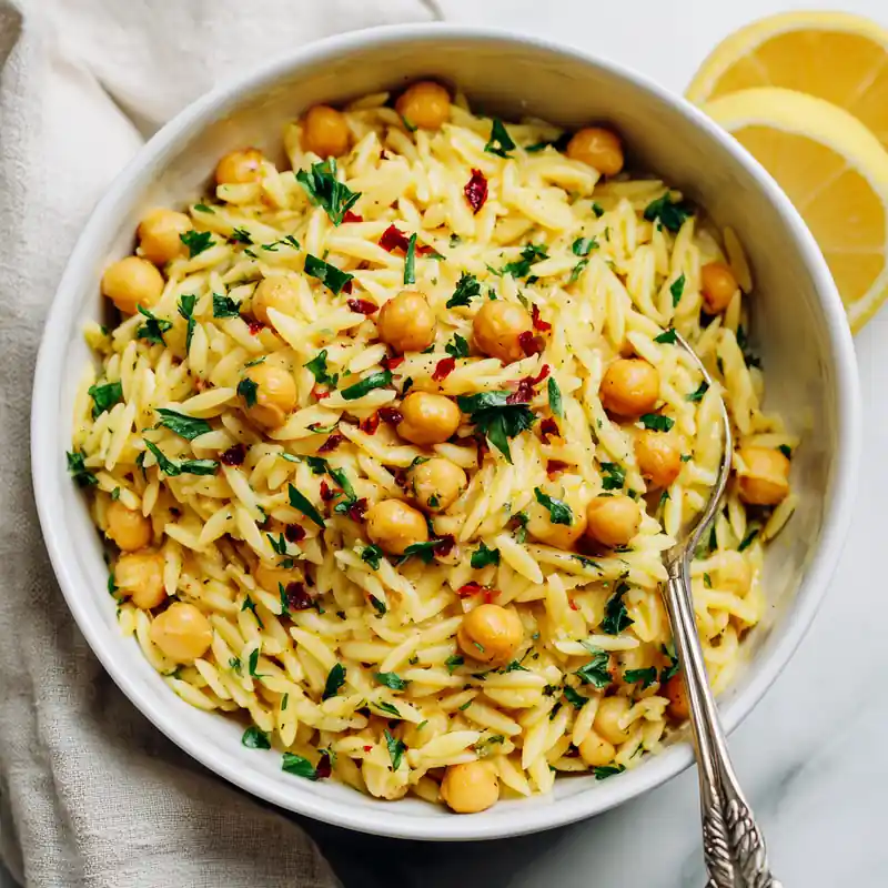 Bowl of creamy lemon chickpea orzo garnished with parsley and chili flakes