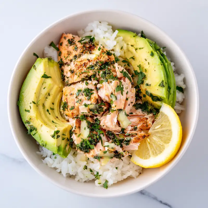 lemon garlic salmon rice bowl with avocado slices, white rice, and fresh parsley in white bowl